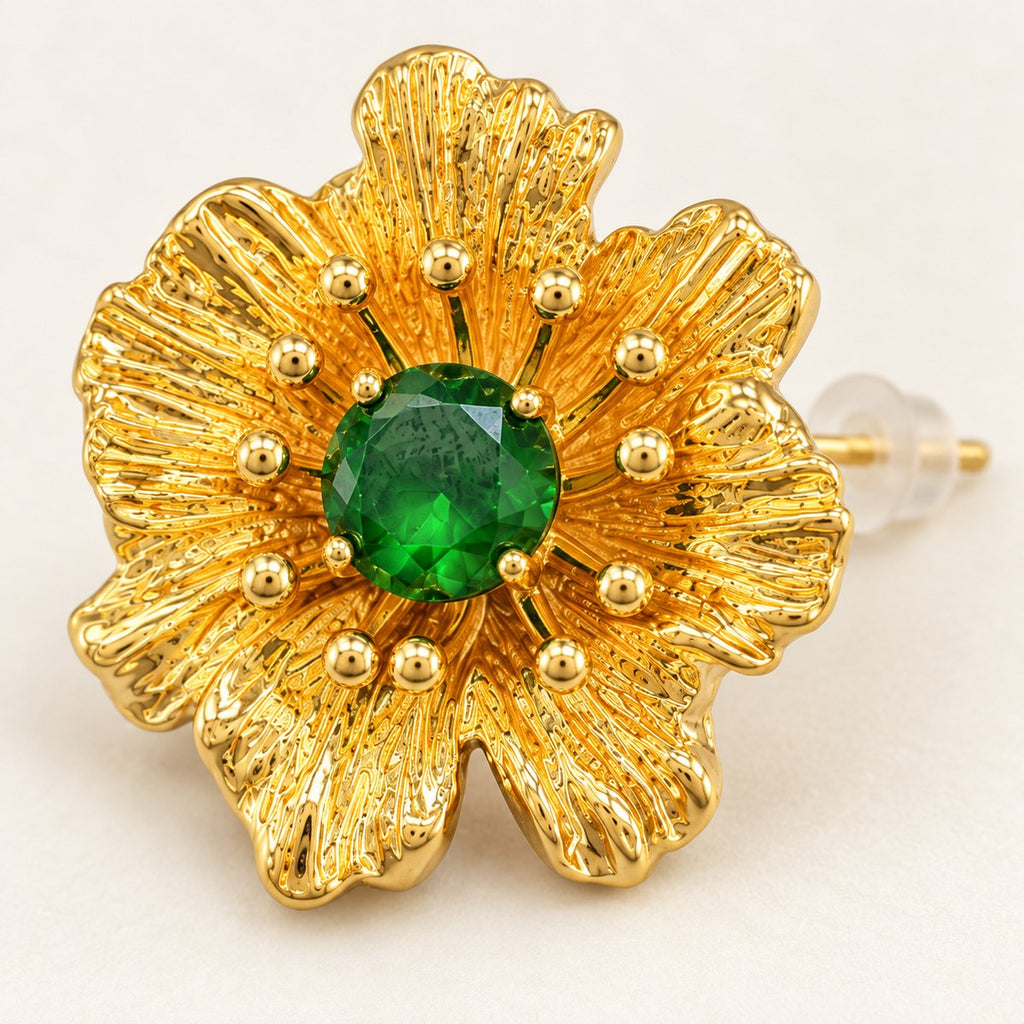 Close-up of textured gold-plated petals, ball-tipped stamens and a faceted green rhinestone