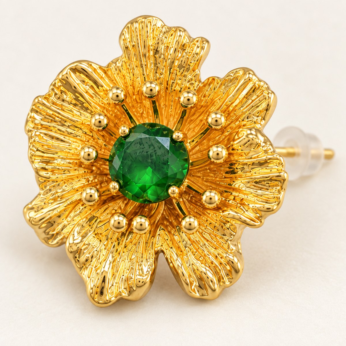 Close-up of textured gold-plated petals, ball-tipped stamens and a faceted green rhinestone