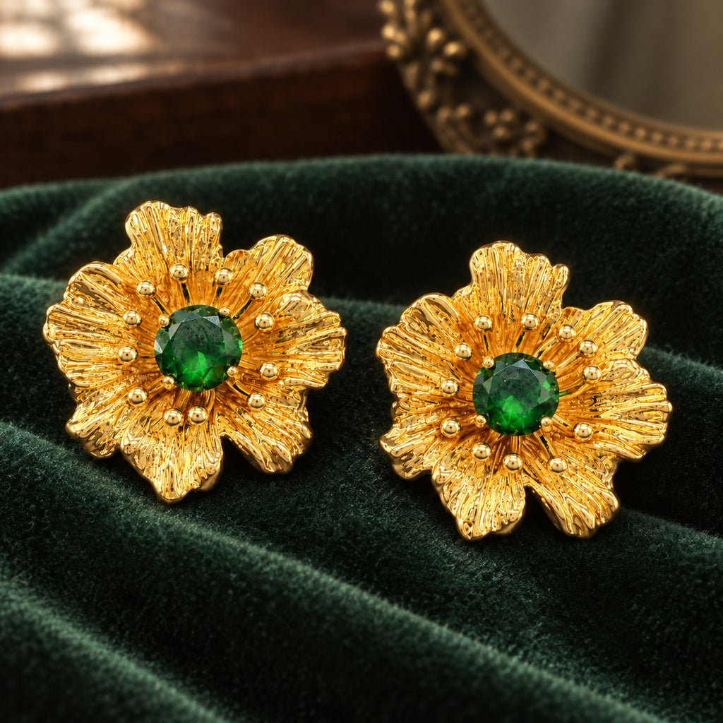 Pair of gold-plated green rhinestone flower stud earrings resting on dark green velvet