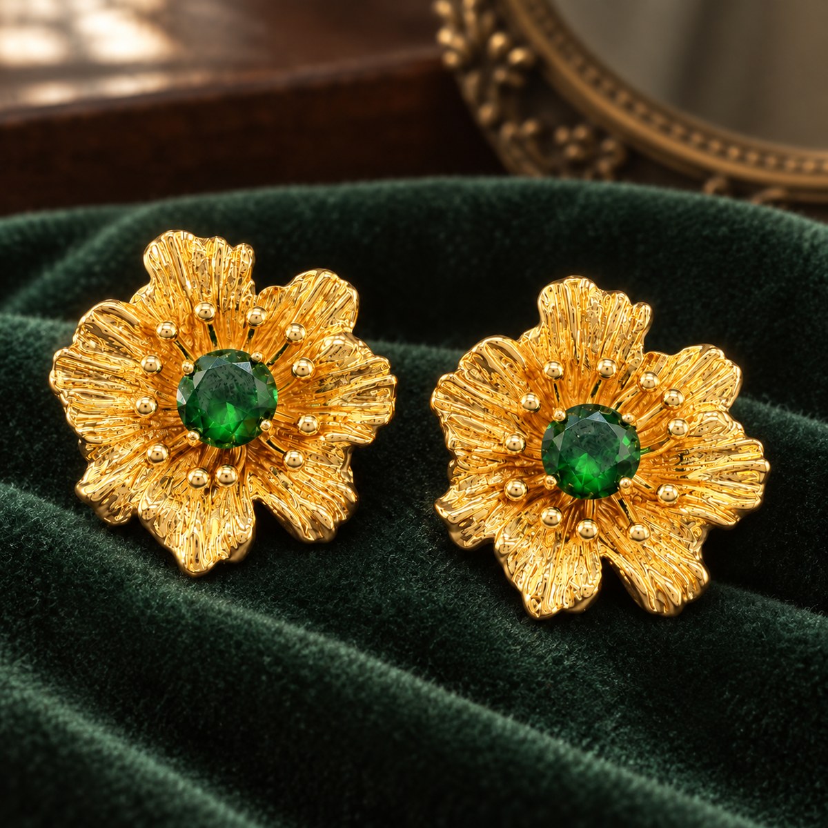 Pair of gold-plated green rhinestone flower stud earrings resting on dark green velvet