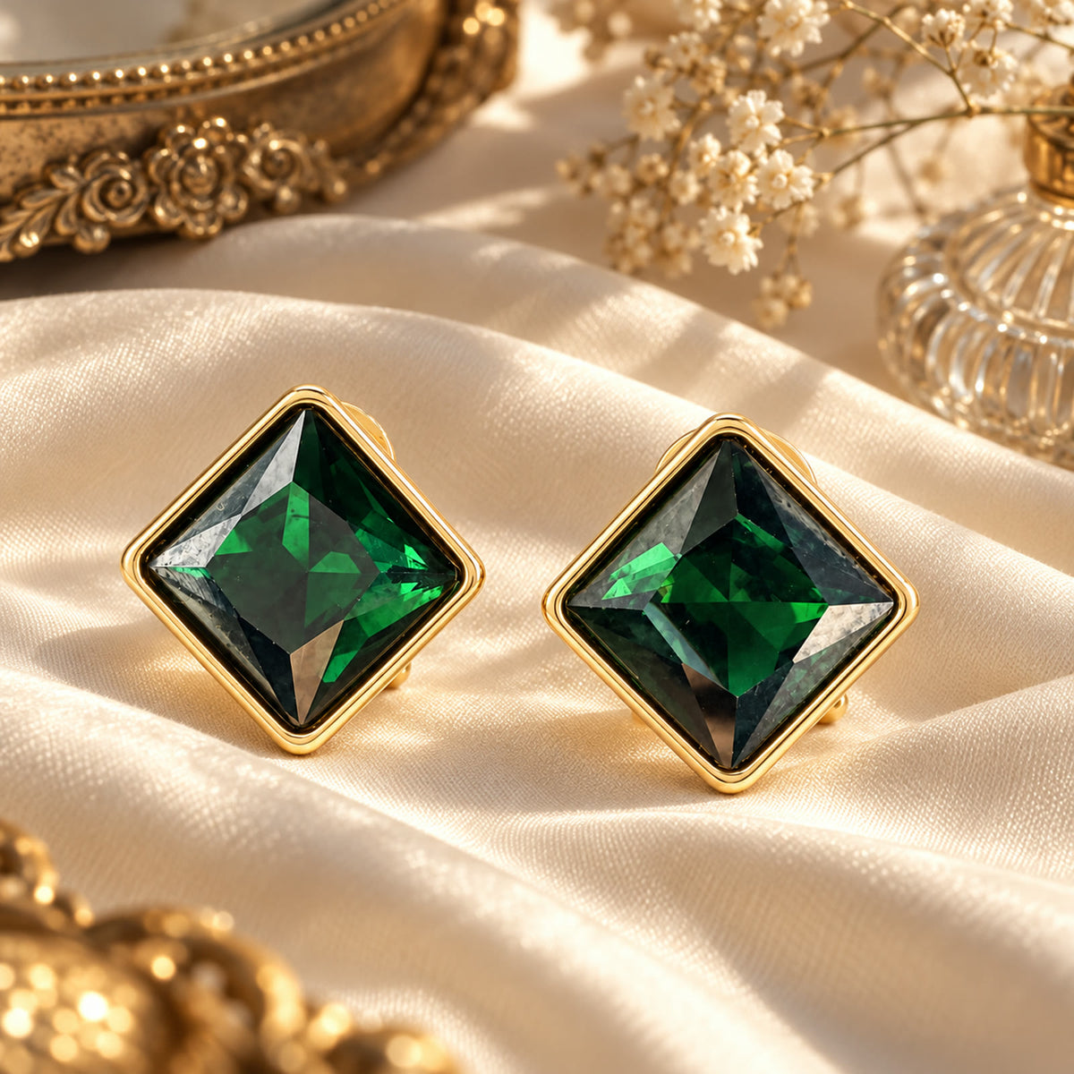 Gold-plated square earrings with green rhinestones styled on cream silk